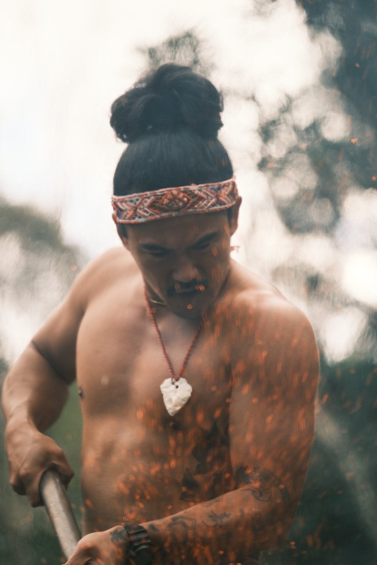 A man in a woven headband tending the fire as embers fly
