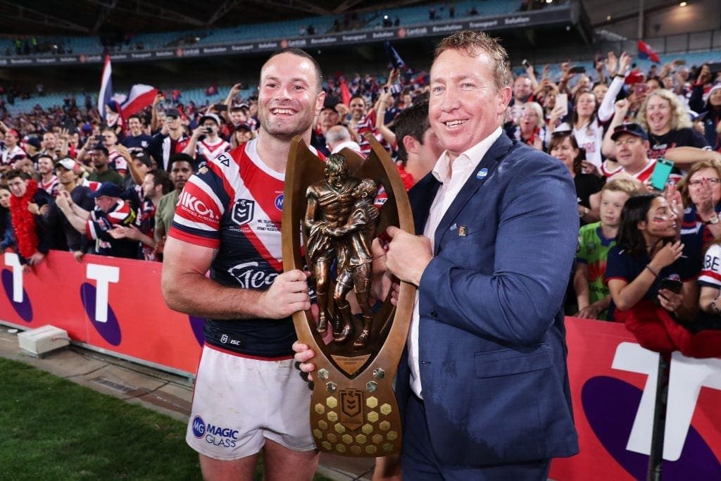 Trent Robinson holding the premiership trophy with a Roosters player in front of the crowd