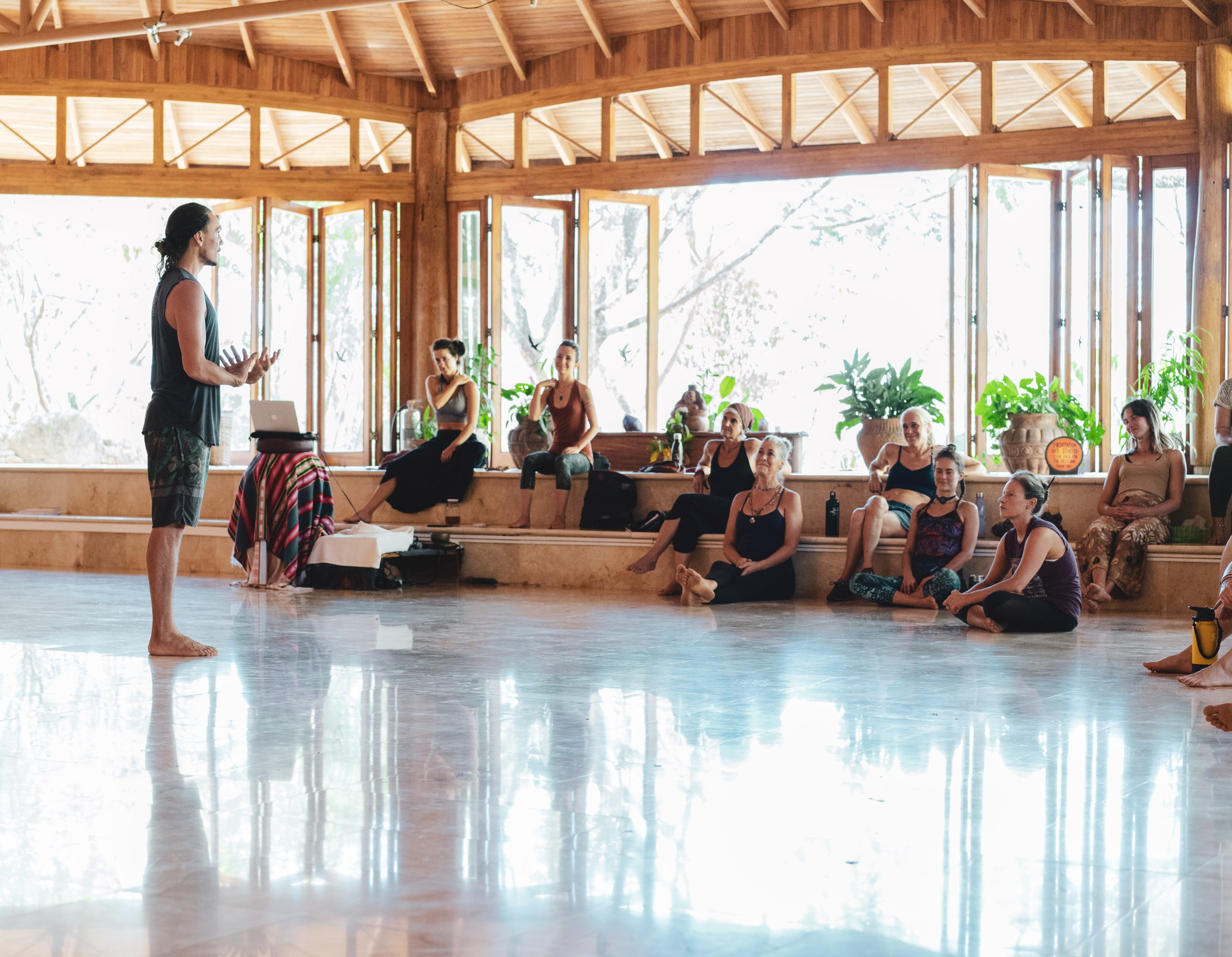 Velan teaching a seated group in an open timber pavilion with a reflective floor