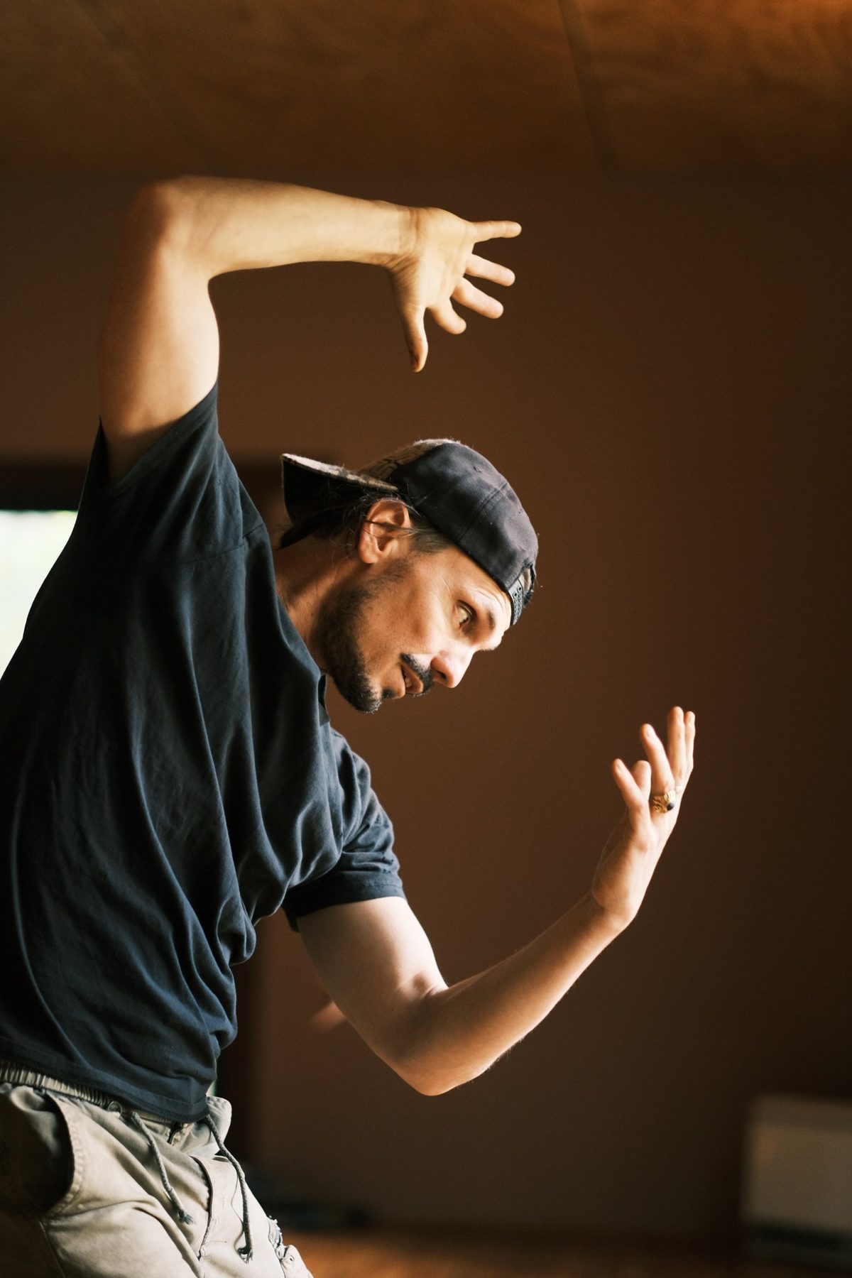 Velan mid-movement, arms raised, in a warm timber room