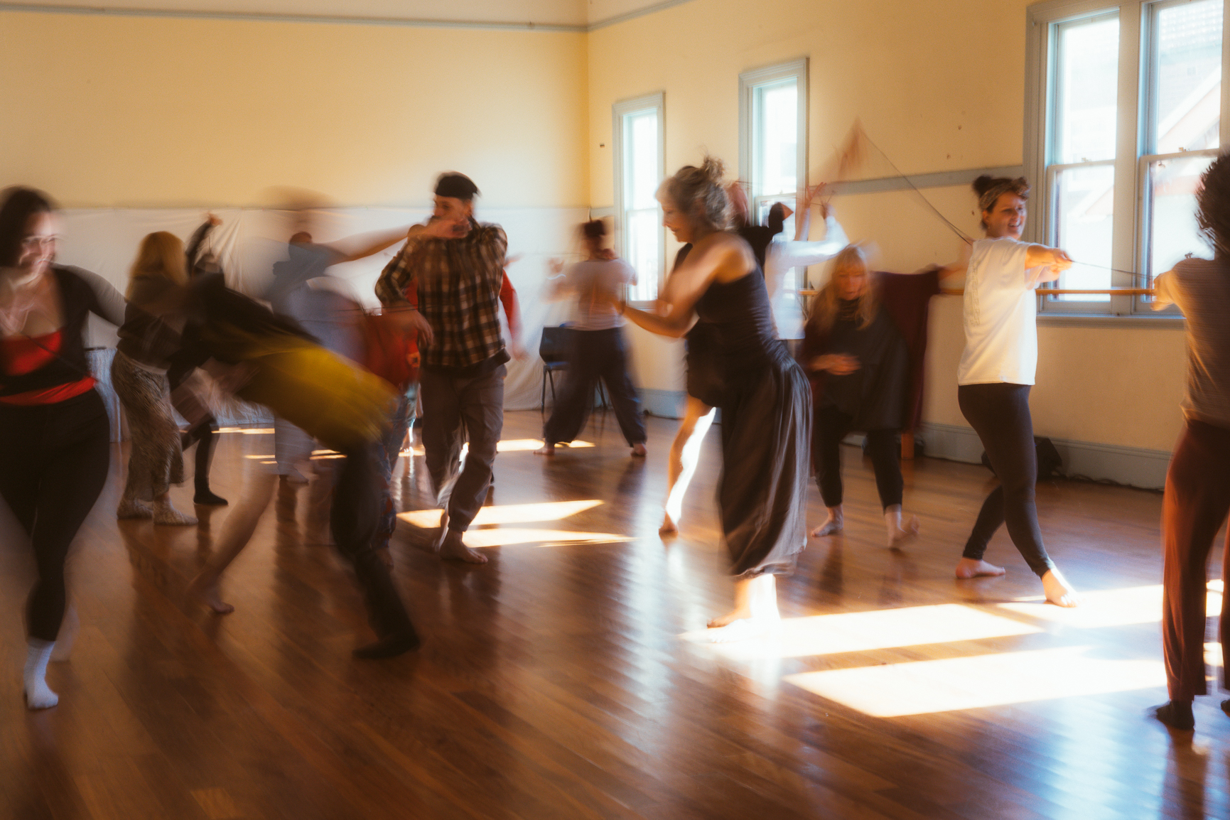 People moving freely through a sunlit timber-floored hall during a movement session