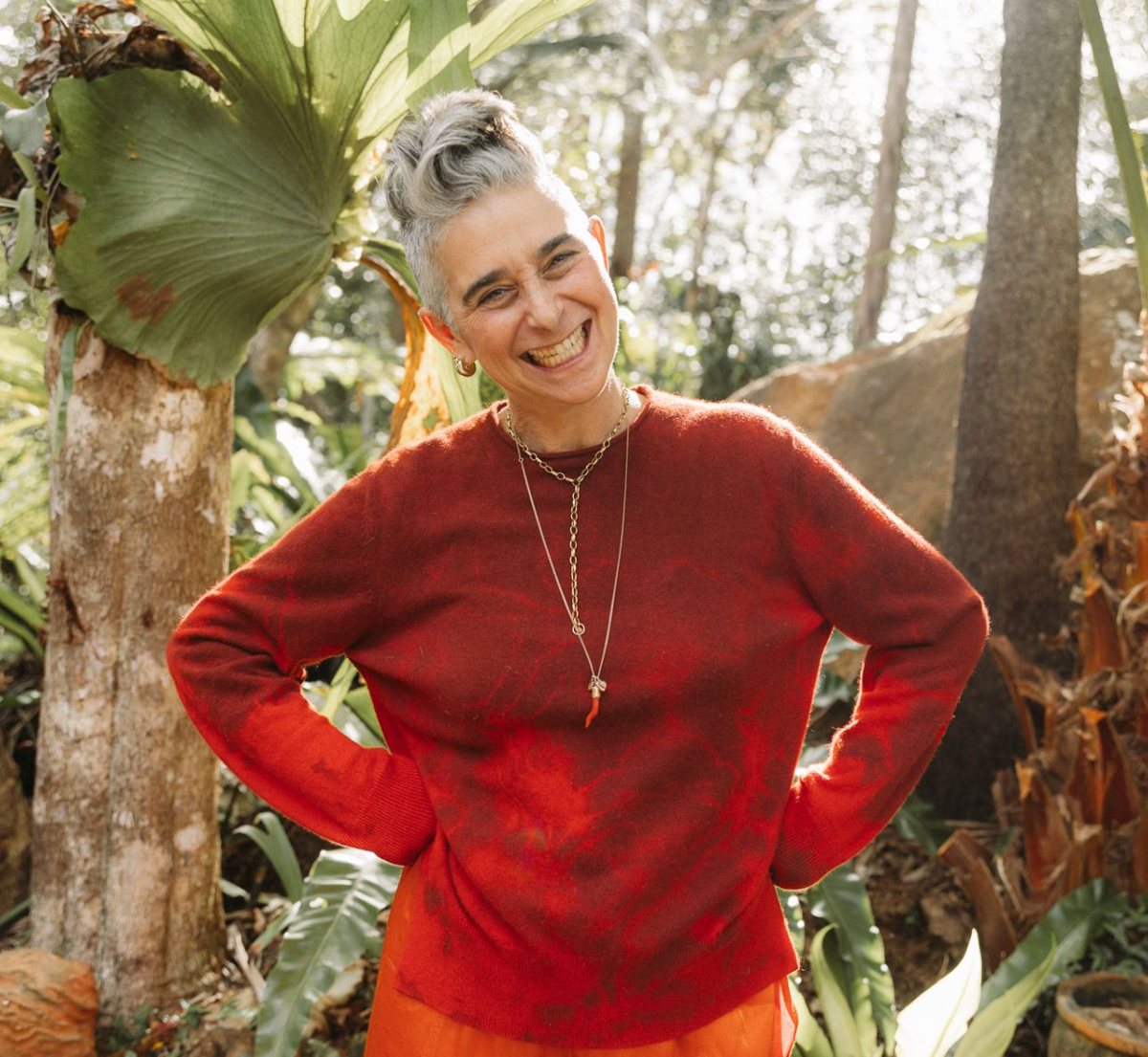 Kate Shela smiling in a red jumper among rainforest plants