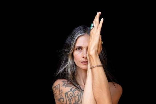 Portrait of Adya, hands raised before her face against a black background