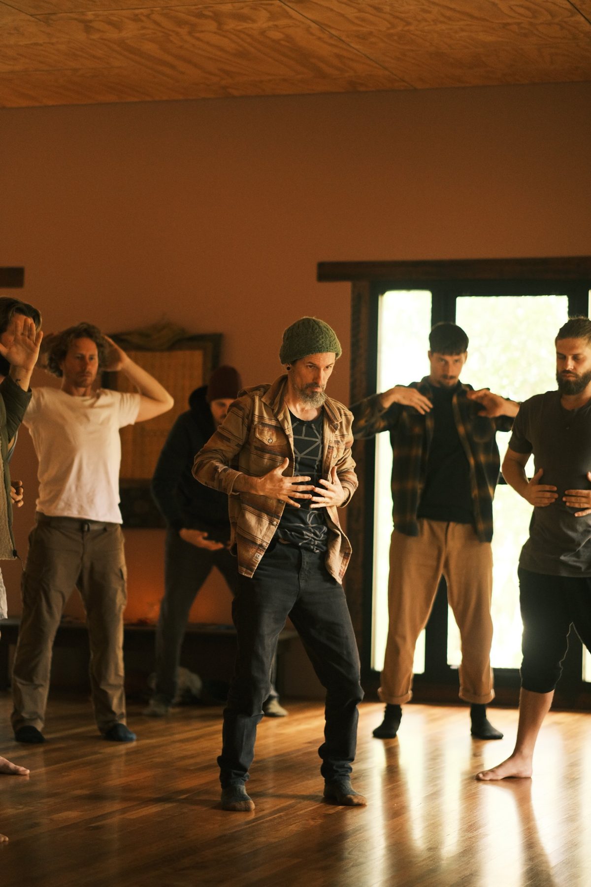 Velan leading a group of men through a somatic practice in the timber retreat hall